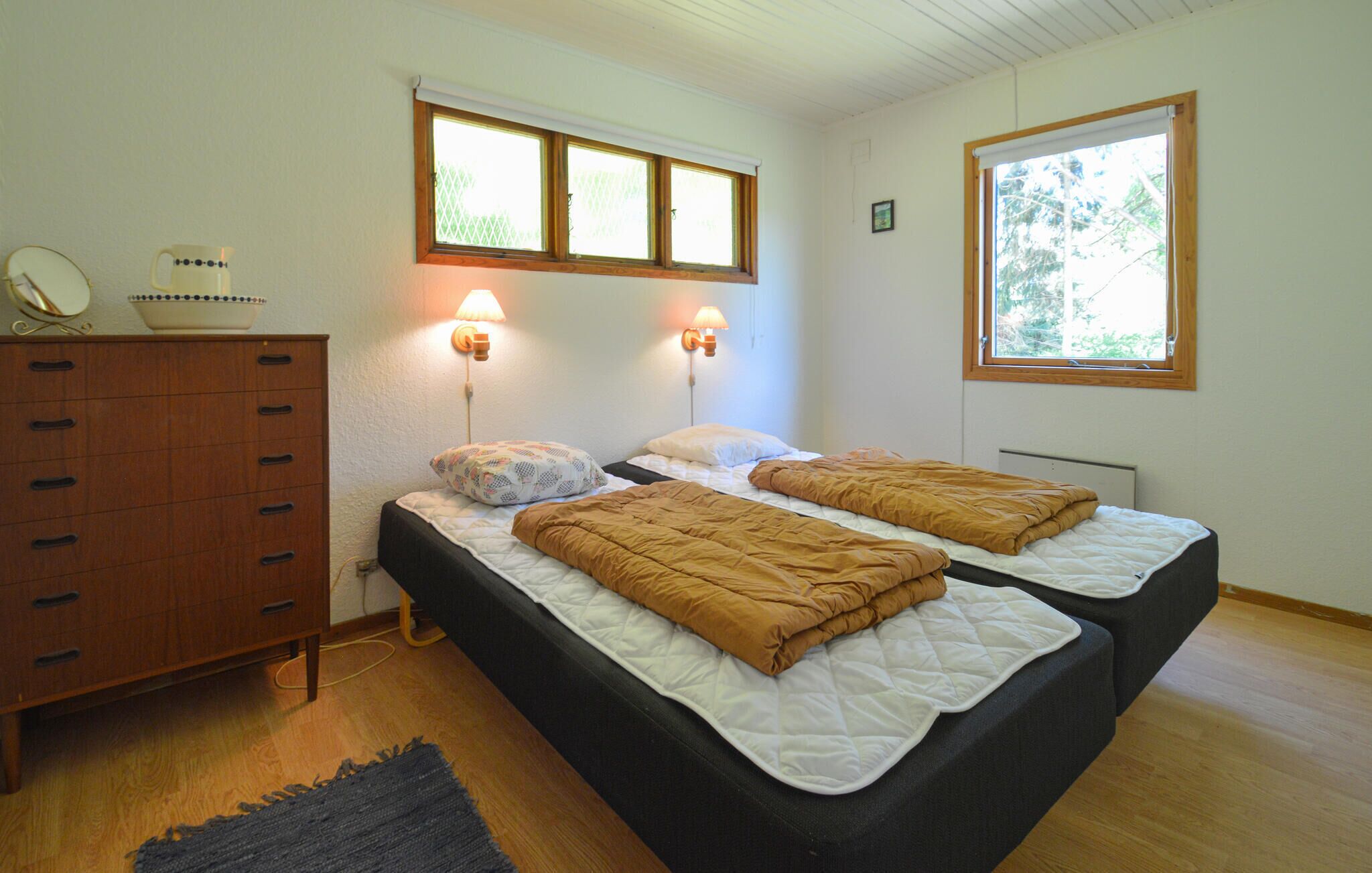 A bedroom with two beds, a wooden dresser, and two wall-mounted lamps.