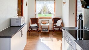 A compact kitchen with a microwave, two wicker chairs, a small table, and a window with curtains.