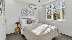 Une chambre moderne avec un grand lit, un ventilateur de plafond et une fenêtre donnant sur la forêt.