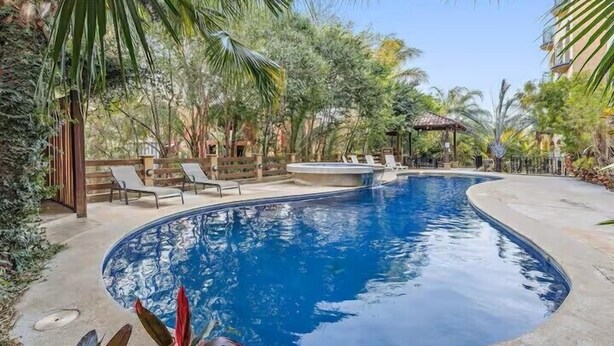 Une piscine entourée de palmiers et de chaises longues, avec un bâtiment en arrière-plan.