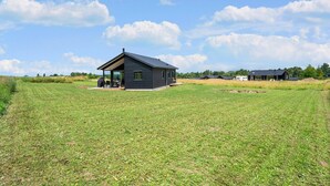 Ein modernes Haus mit Terrasse, umgeben von einer grünen Wiese und blauem Himmel.