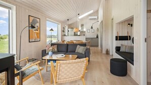 Ein gemütliches Interieur mit einer Couch, einem Esstisch, Stühlen, Holzwänden und einer Küche im Hintergrund.
