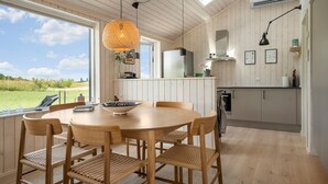 Eine moderne Küche mit Holzausstattung, einem runden Esstisch mit Stühlen und einem großen Fenster mit Blick ins Freie.