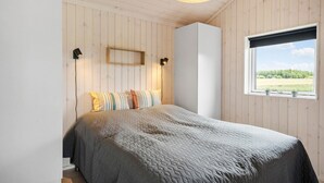 Ein Schlafzimmer mit Bett, Holzwänden, einem Fenster mit Blick und zwei Wandlampen.