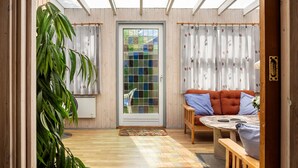 A room with a wooden floor, a glass door with a view, a sofa with cushions, and a plant. - 3 bedroom stunning home in Tarm (Tarm)