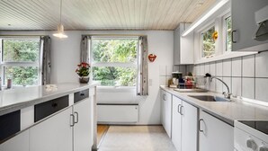 A modern kitchen with white cabinets, a stainless steel sink, and a built-in oven. There are two windows providing natural light, and a potted plant on the counter. - 3 bedroom stunning home in Tarm (Tarm)