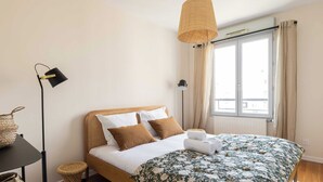 A bedroom with a wooden bed, a large window with curtains, a floor lamp, and a woven basket on a side table. - Dify Republique - Villeurbanne (Villeurbanne)