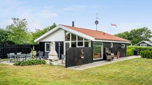 Et hus med en overdækket terrasse, en hegnet baghave og et flag.