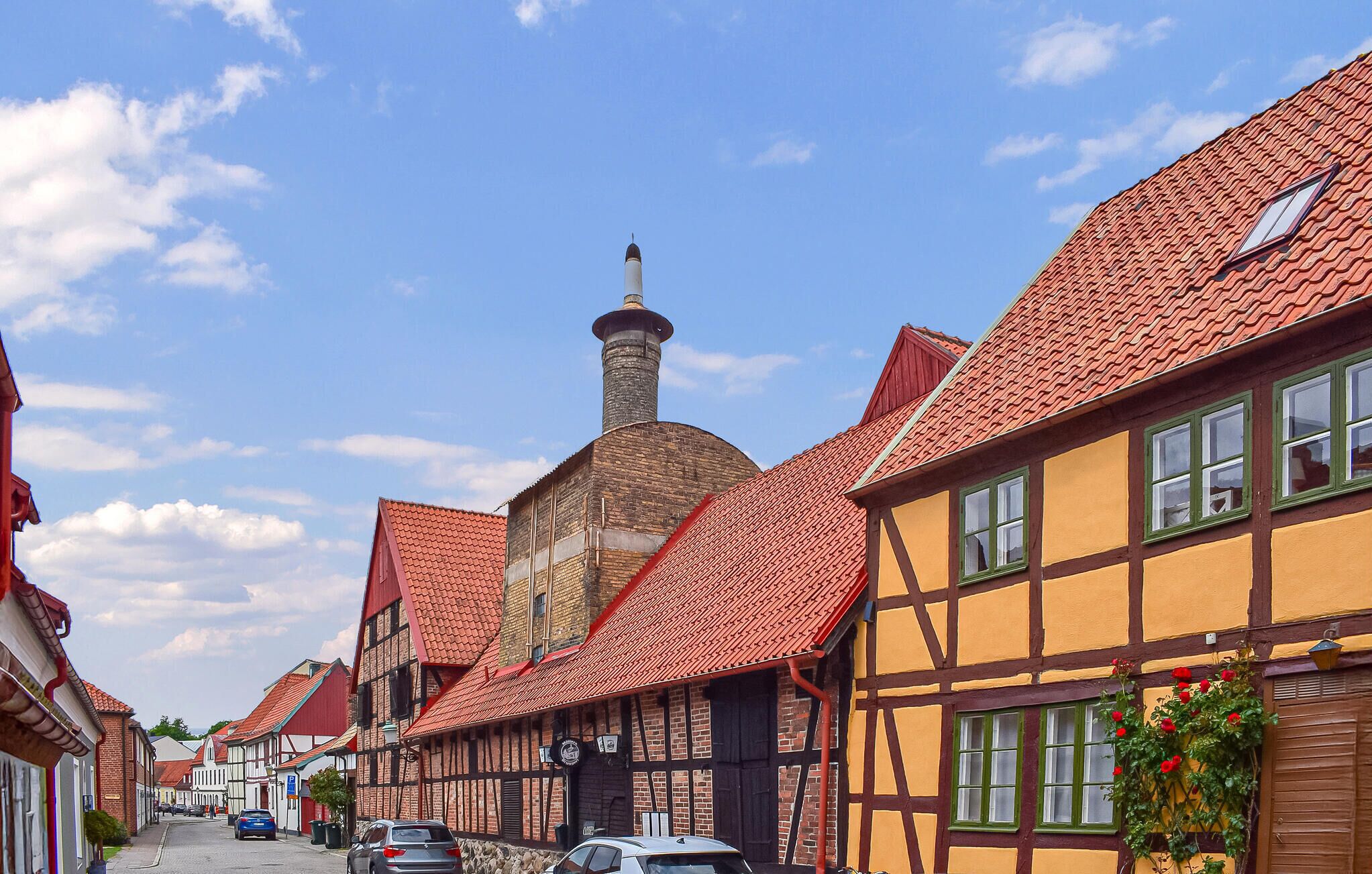 A narrow street lined with traditional half-timbered houses with red tiled roofs and a prominent chimney.
