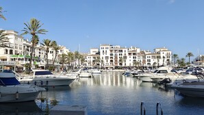 Ein Yachthafen mit mehreren dort vertäuten Booten, umgeben von mehrstöckigen Gebäuden mit Balkonen und Palmen.