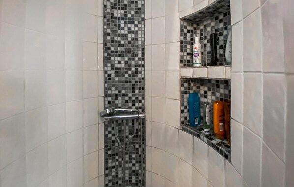 A bathroom with a tiled shower area, a chrome shower door, and a shelf with toiletries. - Cozy home in Kalmar with WiFi (kalmar)