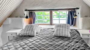 A bedroom with a large bed, two bedside tables, a window with curtains, and a sloped ceiling. - Stunning home in Slite with WiFi (Slite)