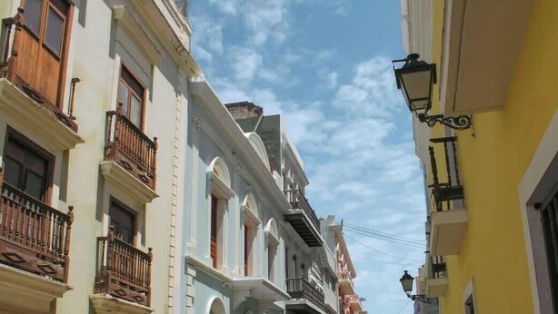 A narrow street with buildings featuring balconies and a street lamp.