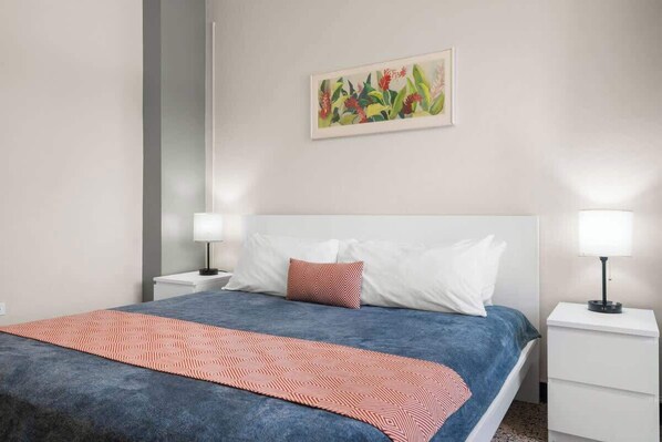 A bedroom with a bed, two bedside tables, and a wall-mounted painting.
