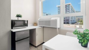 Una kitchenette compacta con microondas, un refrigerador pequeño y una ventana con vista a edificios.