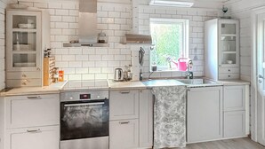 Una cocina moderna con muebles blancos, horno empotrado, ventana con vistas y un lavamanos.