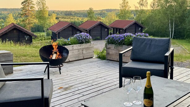 Una terraza de madera con mobiliario exterior, una chimenea y una botella de champán.