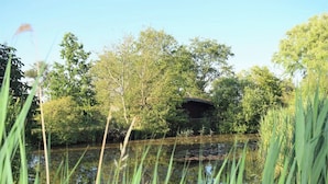 A serene pond with lush greenery and a rustic wooden structure in the background. - Spacious Family-Friendly Apartment with Garden in Ockholm (Ockholm)