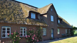 A brick house with a thatched roof, a wooden fence, and pink flowers in the front yard. - Spacious Family-Friendly Apartment with Garden in Ockholm (Ockholm)