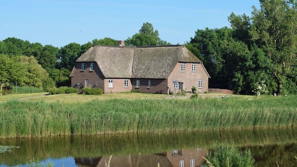 A traditional brick house with a thatched roof, surrounded by a pond and lush greenery. - Spacious Family-Friendly Apartment with Garden in Ockholm (Ockholm)