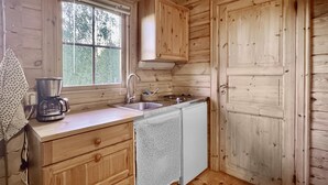 Une cuisine de taille réduite, dotée de meubles en bois, d’un évier, d’une machine à café et d’un lave-vaisselle.