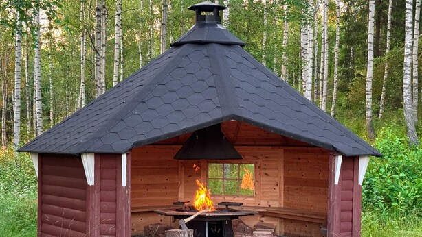 Une cabane en bois dotée d’un toit hexagonal et d’un foyer central.