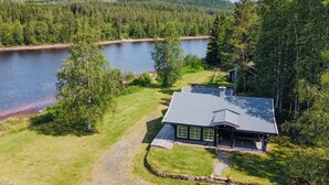 Un chalet au bord du lac, avec des fondations en pierre, entouré d’une végétation luxuriante et offrant une vue dégagée sur le lac.