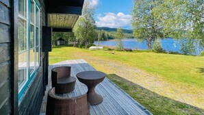 Une terrasse en bois, meublée de mobilier en osier, qui offre une vue sur un lac et une forêt.
