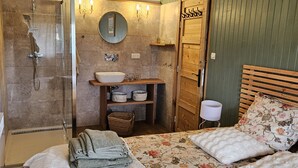 Een slaapkamer met een bed, een nachtkastje, een houten kledingkast, een badkamer met douche, wastafel en spiegel.