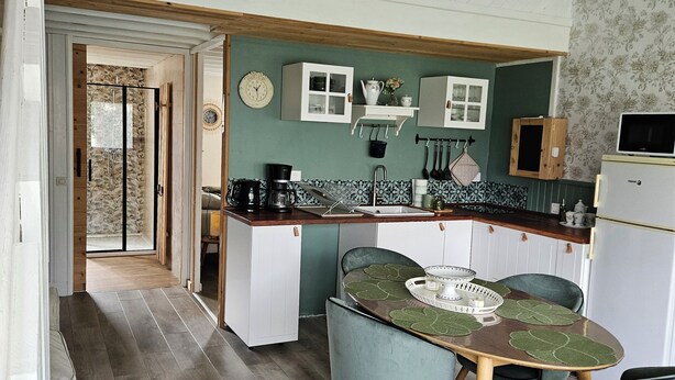 Een moderne keuken met een eetgedeelte, met een houten tafel met stoelen, een hanglamp en een koelkast.