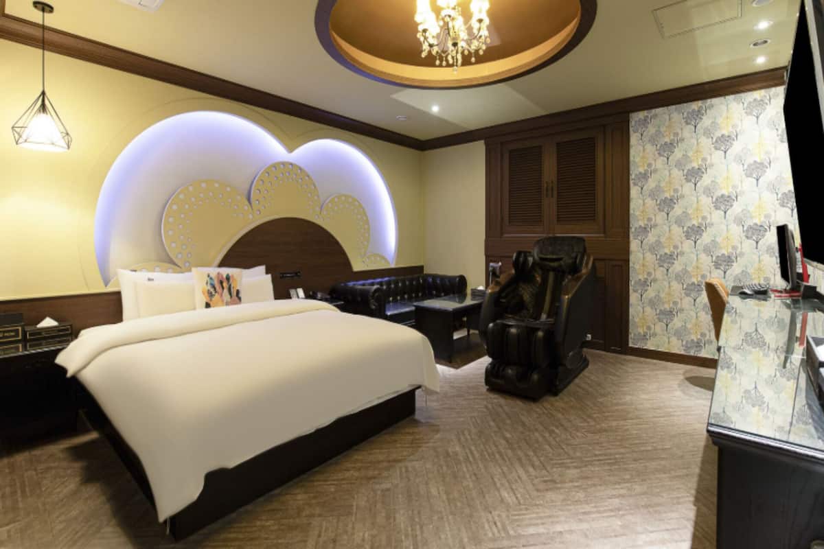 Une chambre d’hôtel dotée d’un grand lit, d’un coin salon avec un fauteuil massant, d’un bureau avec un ordinateur et d’un mur décoratif orné de motifs circulaires.
