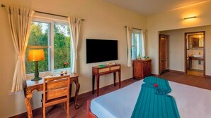 A hotel room with a bed, a desk, a television, and a bathroom visible through an open door. - Sleeping Beauty By Nature Resorts  (Aruvankadu)