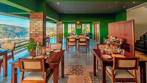 A restaurant with a view of the mountains, wooden tables and chairs, and a green interior. - Sleeping Beauty By Nature Resorts  (Aruvankadu)