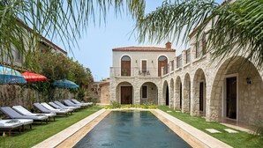 A pool area with lounge chairs and a stone building with arches. - Samsara Alaçatı (Çeşme)