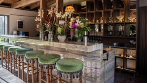 A bar area with a marble countertop, green bar stools, and a variety of flowers and glassware. - Samsara Alaçatı (Çeşme)