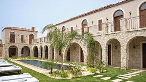A courtyard with a swimming pool, lounge chairs, and a stone building with arched doorways and balconies. - Samsara Alaçatı (Çeşme)