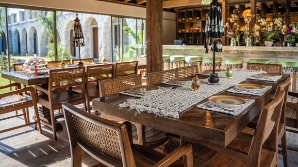 A wooden dining area with tables set for four, surrounded by wicker chairs. - Samsara Alaçatı (Çeşme)