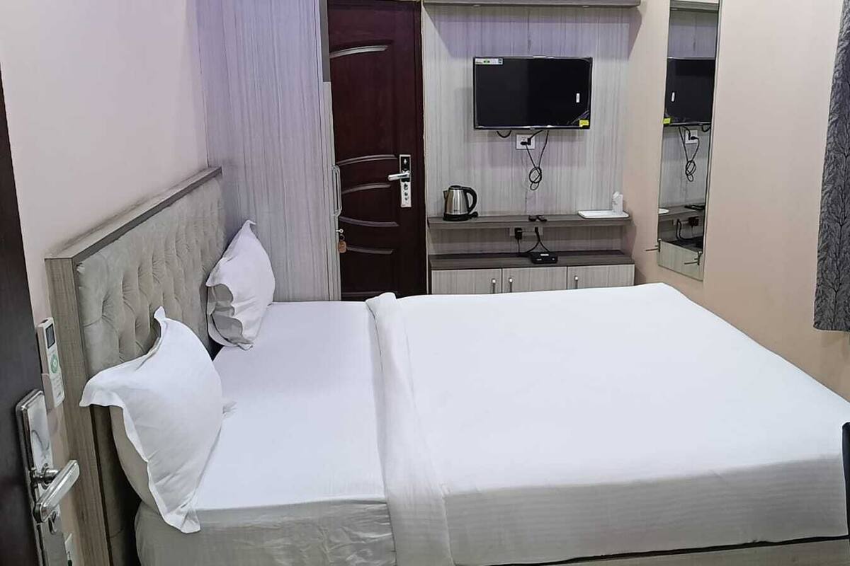 A hotel room with a bed, a TV mounted on the wall, a coffee maker, and a mirror.