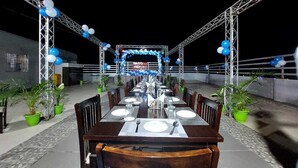 A rooftop dining area with a long table set for a meal, surrounded by potted plants and a metal railing. - HOTEL JD INN (Dumka)