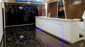 A modern reception area with a marble floor, a white reception desk, and a decorative chandelier. - HOTEL JD INN (Dumka)