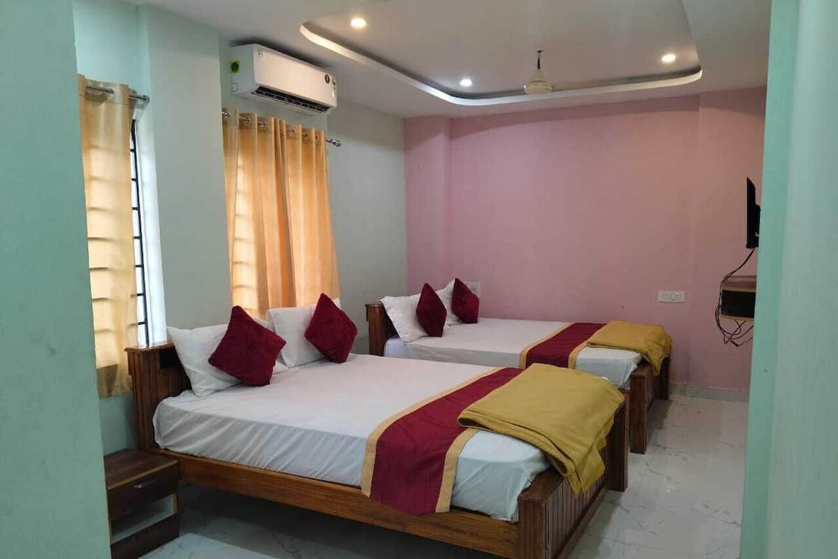 Habitación de hotel con tres camas de madera, cada una con ropa de cama blanca y cojines decorativos rojo y amarillo. Un equipo de aire acondicionado está montado en la pared sobre las camas.