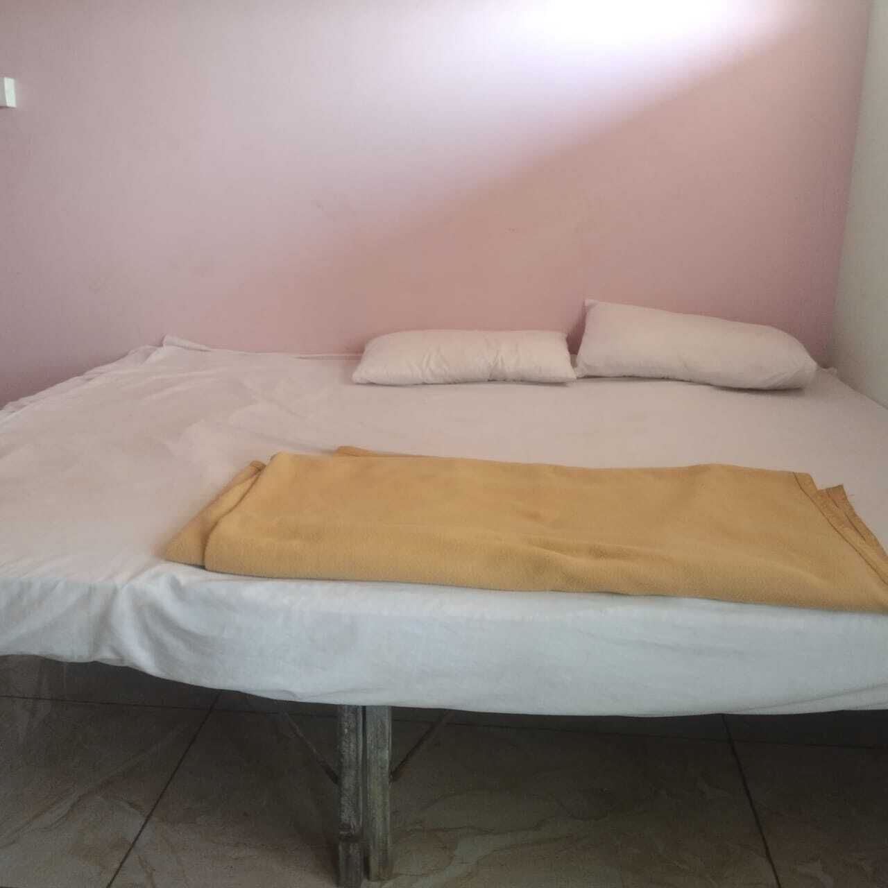 A single bed with white bedding and a yellow blanket, pink walls, and a tiled floor.