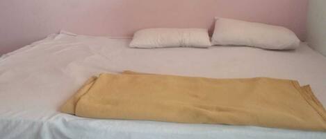 A single bed with white bedding and a yellow blanket, pink walls, and a tiled floor.