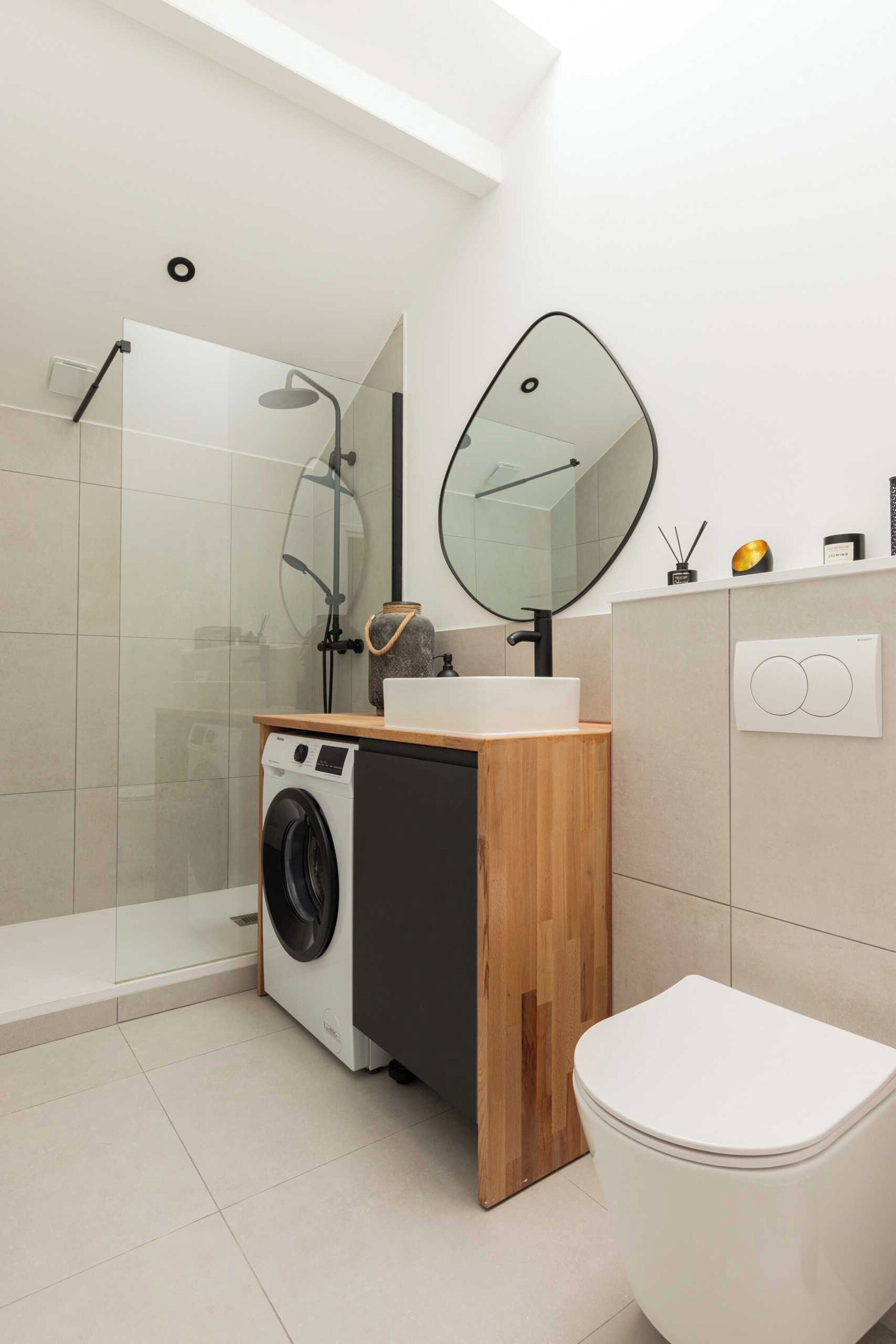 Een moderne badkamer met een douchecabine van glas, een wasmachine, toilet en een houten wastafelmeubel met spiegel.