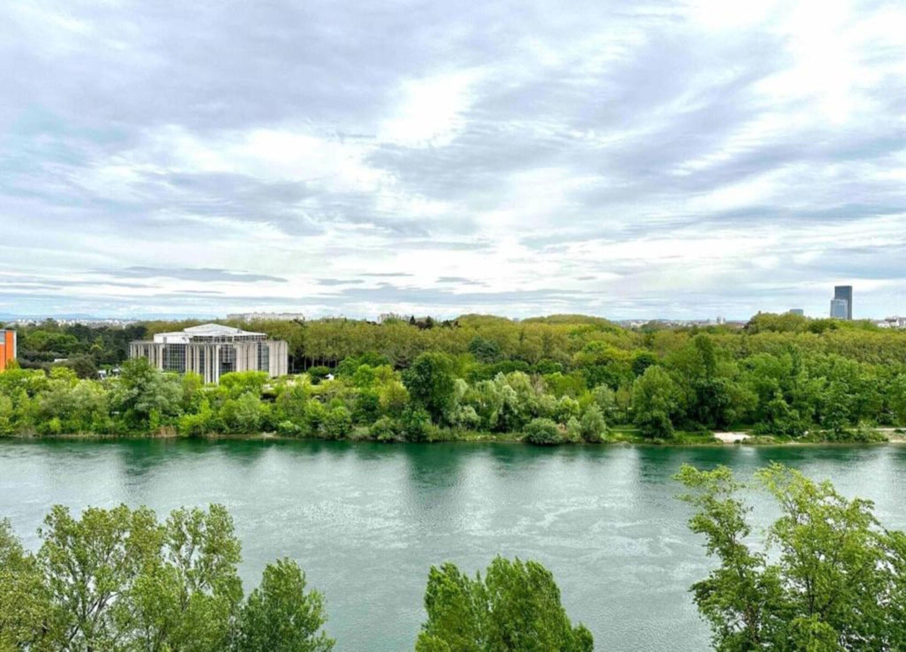A river with a building on the left and a forested hill in the background.