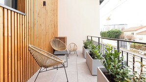 Een balkon met houten latten, twee rieten stoelen en planten in potten.