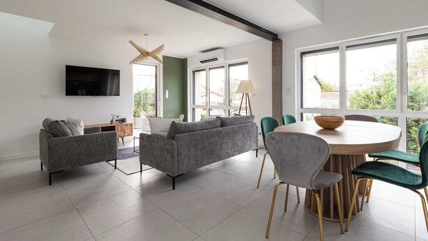 Een moderne woonkamer met een grijze bank, een eettafel met stoelen en een aan de muur bevestigde televisie.