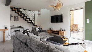 Een moderne woonkamer met een grijze bank, een zwarte salontafel, een houten tv-meubel en een trap met zwarte leuningen.