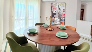 Un comedor con una mesa redonda de madera, sillas verdes y un cuadro abstracto colorido en la pared.