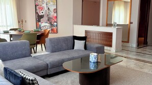 Una sala de estar moderna con un sofá gris, una mesa de centro de vidrio y un comedor con mesa preparada para cuatro.